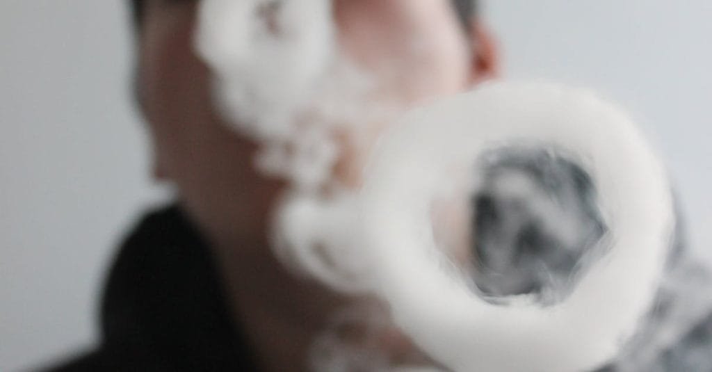 A man creating smoke rings indoors, photographed in a low angle shot with selective focus.